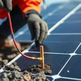 Técnico instalando haste de aterramento de cobre ao lado de inversor solar montado em parede externa
