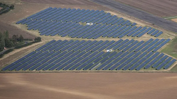 Vista aérea de usina fotovoltaica com painéis solares enfileirados sob céu parcialmente nublado