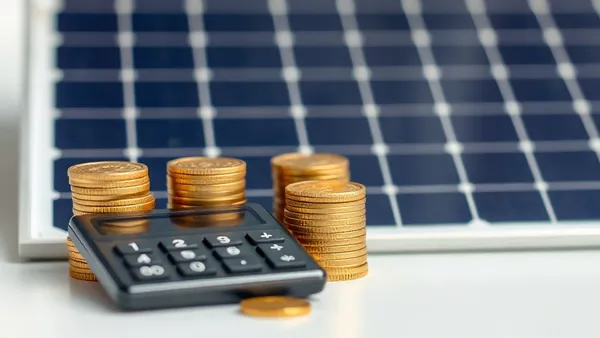 Calculadora, moedas e painel solar representando o cálculo do payback de energia solar por distribuidora