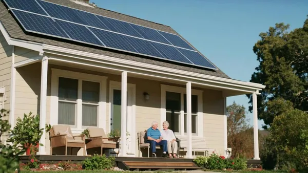 Casal de idosos sentado na varanda de uma casa com painéis solares no telhado